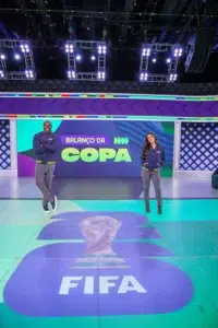 Carol Barcellos no palco do Balanço da Copa, com o logo da FIFA