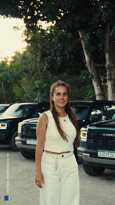 Carol Barcellos em pé diante de veículos GWM Haval estacionados em uma área arborizada.